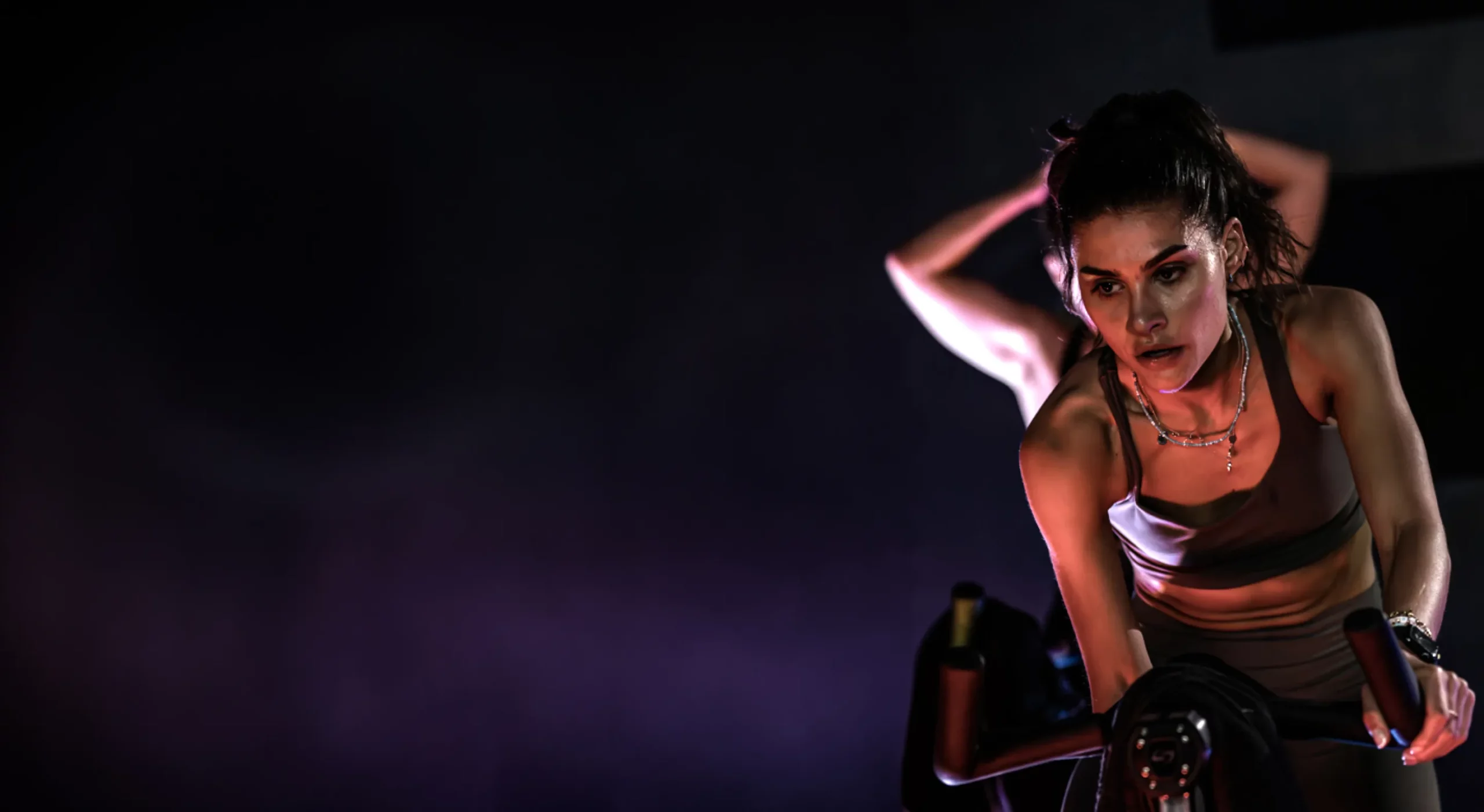 Woman riding a stationary bike in a dark Boom Cycle spin class, intensely focused under dramatic purple lighting.