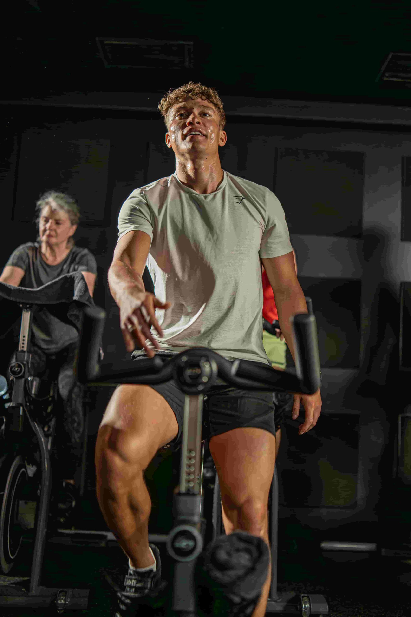 Focused man mid-ride in a Boom Cycle indoor cycling class, sweating and pushing through an intense workout with other riders in the background.