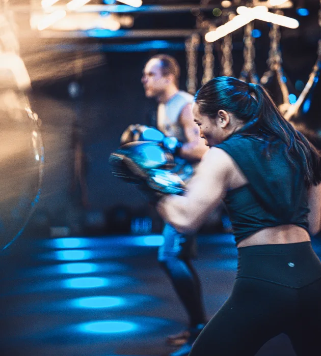 KOBOX client throwing punches during a high-intensity boxing and HIIT class, set in a nightclub-inspired studio with immersive lighting and energy.